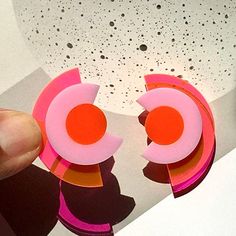 "Deconstruct your style with these modern geometric studs. A modern take on the Art Deco aesthetic, these abstracted eyes in a concentric arrangement will add color blocking to your outfit. Bold with a neon pink/orange backing, these earrings project a bright light effect that is sure to make a statement. Made from 1/8\" thick acrylic, these earrings are made of solid construction with a mixture of solid and clear acrylic pieces that let light through. Each earring measures approximately 1-3/8 i Bold Geometric Earrings With Bold Design, Bold Geometric Designed Earrings, Modern Handmade Geometric Earrings, Handmade Modern Geometric Earrings, Pink Geometric Earrings, Modern Multicolor Earrings With Bold Design, Modern Geometric Earrings, Bold Geometric Earrings, Bold Handmade Geometric Earrings