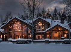 a large house with lots of windows and lights on in the snow covered yard area