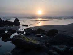 the sun is setting over some rocks on the beach