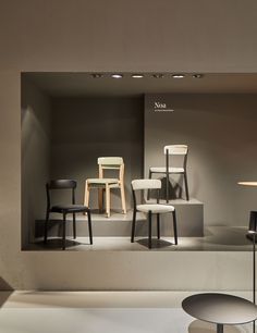 several chairs and tables on display in a room with light from the window behind them