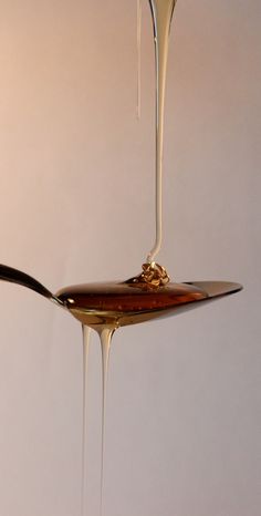 a spoon with liquid dripping from it on top of a white table next to a wall