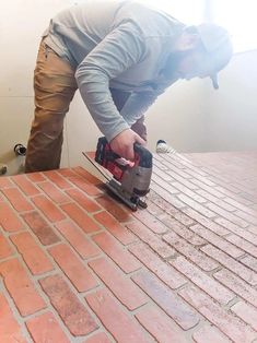 a man sanding bricks with a power tool on top of the brick floor in front of him