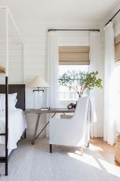 a bedroom with white walls and wood flooring has a canopy bed, two chairs, and a small table with a potted plant on it