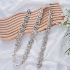 two bridal bracelets on top of a white cloth next to flowers and a wooden board