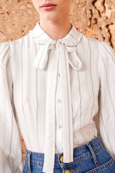 A feminine take on classic shirting, the Vedra Blouse is a timeless silhouette in white silk with delicate stripes that feature jacquard threads for added texture. This romantic top is adorned with a slightly ruffled collar, tapered sleeves with buttoned cuffs, and a removable bow at the neckline. It fastens with buttons down the center front. Fit Note: This style runs slim, we recommend sizing up for a more relaxed fit. Composition: 100% Silk Pair with our Lou Jean and Mini Floret Stud to compl Elegant White Top With Striped Collar, Elegant Striped Blouse, Elegant White Blouse With Striped Collar, Elegant Striped Blouse For Spring, Classic Formal Blouse With Striped Collar, Elegant Blouse With Striped Collar For Daywear, Elegant Formal Top With Striped Collar, Elegant Striped Formal Tops, Elegant Formal Tops With Striped Collar