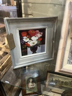 framed pictures and flowers are on display in a glass case