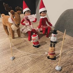 three elfs sitting on top of a wooden table next to a snowman and reindeer