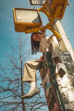 a woman is hanging off the side of a street light pole with her feet up