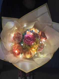 a bouquet of flowers with lights in the middle is being held by someone's hand