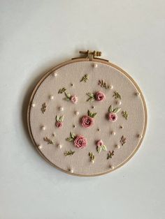 an embroidery project with pink flowers and pearls on the hoop, hanging from a white wall