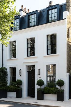 a white two story house with black shutters and potted plants on the sidewalk