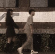 two people walking down the street in front of a train