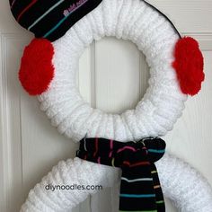 a white knitted wreath with red and black pom - poms