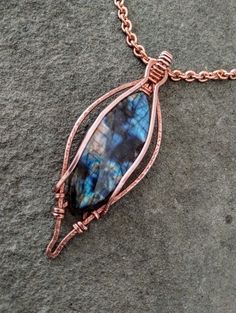 a wire wrapped pendant with a blue stone in the center on a rock surface,