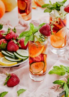 two glasses filled with fruit and ice on top of a table next to sliced lemons