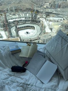 an open book on top of a bed next to a pillow and other items in front of a window