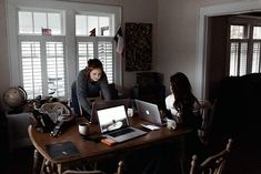 two women sitting at a desk with laptops and papers in front of their faces