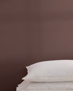 three pillows stacked on top of each other in front of a brown wall with white sheets