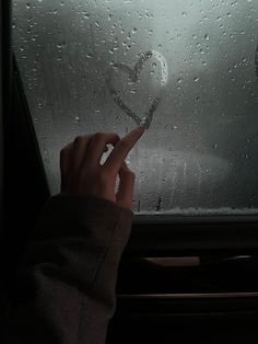 a person is holding their finger up in front of a window with rain drops on it