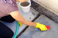 a woman in yellow gloves is cleaning the sidewalk with a bucket and water hoses