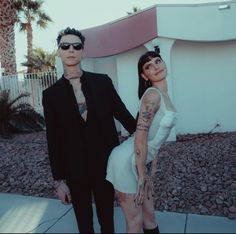 a man and woman standing next to each other in front of a white building with palm trees