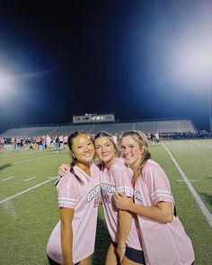 three girls in pink uniforms posing for the camera on a soccer field at night time