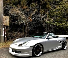 a silver sports car is parked on the side of the road in front of some trees