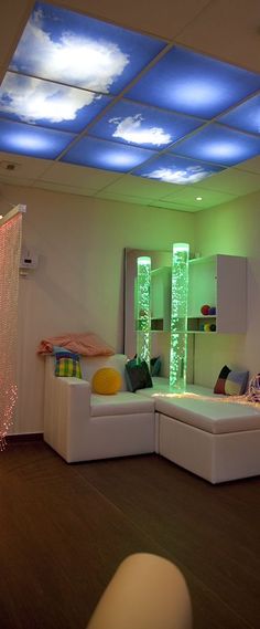 a living room filled with white furniture and colorful lights on the ceiling above it's windows