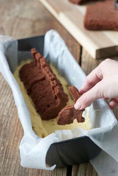 someone is dipping something into some kind of chocolate cake in a baking pan on a wooden table