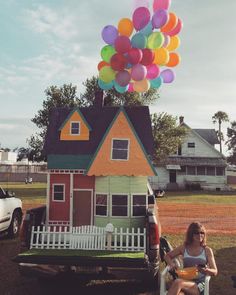 a woman sitting in a chair next to a house with balloons on top