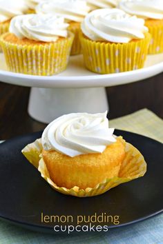 lemon pudding cupcakes with white frosting on a black plate next to a cake stand