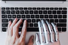 a person typing on a laptop with four robotic hands next to the keyboard and mouse