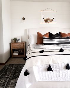 a white bed with black and brown pillows in a bedroom next to a wall mounted antelope