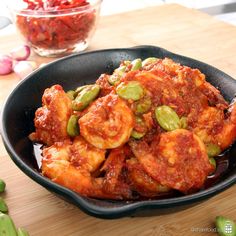 a skillet filled with shrimp and vegetables on top of a wooden cutting board next to red peppers