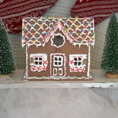 a gingerbread house decorated with icing and candy canes on a shelf next to christmas trees