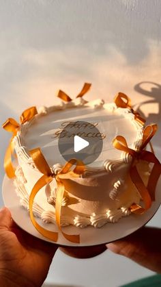 a person holding a cake with orange ribbons on it