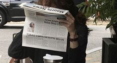 a woman reading a newspaper while sitting at a table with a coffee cup on it