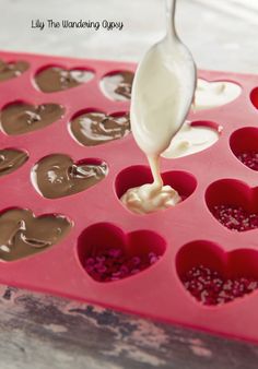 a spoon is pouring chocolate into the heart shaped cupcake pan with hearts on it