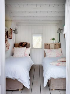 two beds in a small room with white walls and wood flooring, one has pink flowers on them