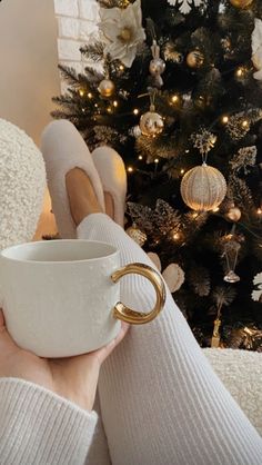 a woman holding a coffee cup in front of a christmas tree with her feet up