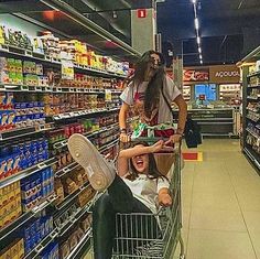 a woman pushing a shopping cart in a grocery store with a man sitting on it