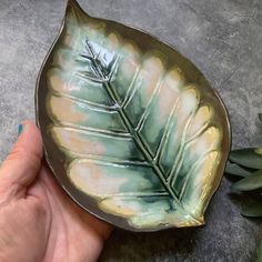 a hand holding a green leaf shaped dish