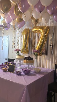 a table topped with balloons and cake next to a number seventy sign hanging from the ceiling