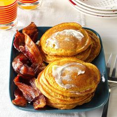 pancakes with bacon and maple syrup on a blue plate next to glasses of orange juice