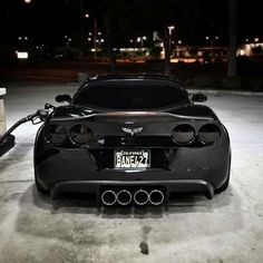 a black sports car parked in a parking lot with its hood up and exhaust pipe out