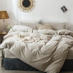 an unmade bed in a white room with a sun decoration on the wall above it