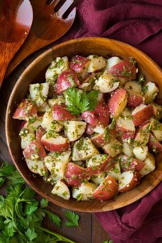 a wooden bowl filled with potato salad next to some parsley on a purple cloth