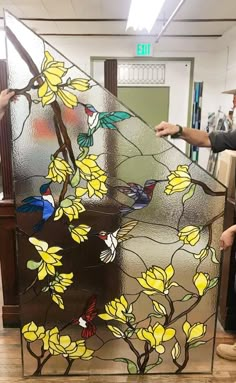 a stained glass window with yellow flowers and birds on it, being held up by two hands