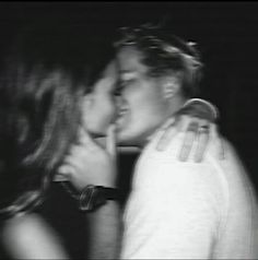 black and white photograph of two people kissing each other in front of a dark background