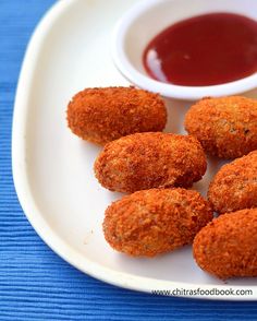 some fried food on a white plate with ketchup and dipping sauce in the background